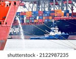 Small photo of Rotterdam, The Netherlands - June 2021; compressed view of harbour activity in the container terminal, with moored ship in forefront pumping out water and blue tug boat midships the container ship