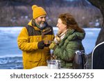 Romantic mature couple family outreach with hot wine near camper. Mature couple enjoying mulled wine in winter romantic tour camping adventure. Family adventure and vacation concept. 