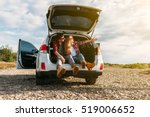 Happy traveler couple sitting in car open trunk and watch the sunrise