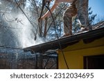 Small photo of Worker standing on the roof and cleaning rain gutter with high pressure water jet. Professional using equipment for roof gutter cleaning. Maintenance and housekeeping concept of drainage channel.