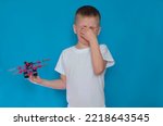 Small photo of A sad, upset little boy is crying on a blue insulated background and holding an airplane in his hands. The child is hysterical because he broke his favorite toy.