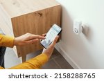 Small photo of Woman setting a smart plug at home using her smartphone, smart home and domotics concept