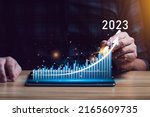 Businessman planning 2023 business growth on desk with virtual hologram chart graph. Calculate income and profit on investments and an increase in the indicators of positive growth