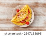 An omelet with tomato and parsley, eggs for breakfast, a healthy vegetarian omelette with cheese, overhead flat lay shot on a rustic wooden background