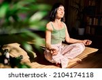 Woman practicing yoga and meditation at home sitting in lotus pose on yoga mat, relaxed with closed eyes. Mindful meditation concept. Wellbeing.