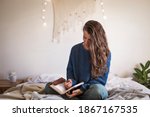 Woman in blue sweater sat on her bed writing in her leatherbound journal