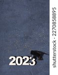 Small photo of Class of 2023 concept. Wooden number 2023 with graduate statuette on concrete background with tinsel top view.