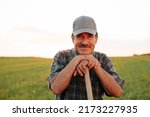 Old farmer with mustache handsome man looking at camera, male satisfied resting at sunset. the portrait of the worker in the agricultural field