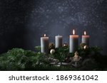 Third advent with three burning candles on fir branches with Christmas decoration against a dark grey background, copy space, selected focus, narrow depth of field