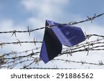 Small photo of refugee labeled passport folded as a paper plane get stuck in the barbed wire of the border against the blue sky with white clouds, copy space