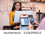 Small photo of Asian women Barista smiling and using coffee machine in coffee shop counter and Asian customer women paying by QR code scanning on mobile phone at shop