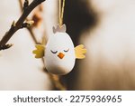 Easter egg in a form of a cute chicken hanging on a branch of a flowering tree in a spring garden in sunny day. Easter wallpaper for desktop. Greeting card. Decor for a springtime religious holiday. 