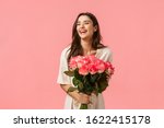 Valentines day, romance, celebration and beauty concept. Charming elegant and feminine young woman receive flowers, holding beautiful bouquet and laughing joyfully, pink background