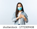 Social distancing lifestyle, covid-19 pandemic everyday life and leisure concept. Delighted happy asian girl being praised, feeling touched and thankful, touching heart, smiling in medical mask