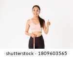 Small photo of Fitness, healthy lifestyle and wellbeing concept. Portrait of satisfied smiling, cute asian girl in sportswear, showing thumbs-up after measuring waist with tape measure, lost weight