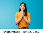 Small photo of Upset cute silly asian girl praying, plead for help, pouting frowning need, make pitty face, hold hands pray begging for favor, apologizing feelings guilty sad, stand blue background