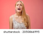 Small photo of Immature whining spoiled adult rich daughter blond long hair in silver stylish dress complaining sad cruel unfair life crying sobbing frowning sulking upset, standing disappointed red background