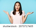 Confused asian girl spread empty hands sideways, shrugging shoulders clueless, standing in tshirt over blue background