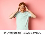 Small photo of Portrait of redhead man in crooked glasses touching head and feeling dizzy or nauseous, having hangover or headache, standing over pink background