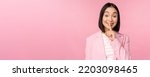 Small photo of Hush, taboo concept. Portrait of asian businesswoman showing shush gesture, shhh sign, press finger to lips, standing over pink background in suit