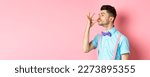 Small photo of Profile of funny guy touching his french moustache and pucker lips like snob, standing smug on pink background and look left.