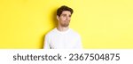 Small photo of Reluctant guy in white t-shirt looking left, grimacing skeptical and displeased, standing over yellow background.