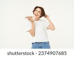 Small photo of Portrait of chatty woman talking in speakerphone, records voice message on mobile phone and smiling, stands over white background.