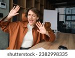 Portrait of female employee, start up manager in office dancing, sitting and listening to music in wireless headphones, singing along her favourite song.