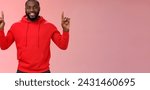 Small photo of Devious cute african-american bearded guy in red hoodie smiling mysterious know exactly what you want pointing raised index fingers up grinning show perfect copy space promo, pink background.