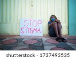 Small photo of Young black woman wearing a locally made mask, sitting outdoors with campaign sign on stop covid-19 (corona virus) stigma - concept on infected people with covid-19 and stigmatization( social stigma )