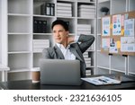 Small photo of Overworked young Asian businessman office worker suffering from neck pain after had a long day at office desk. office syndrome concept