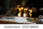 Small photo of The waiter serves the couple their main course and wine while they wait for their order in the luxury restaurant. Candles lit near the dining table provide a dim and pleasant atmosphere.