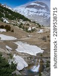 Small photo of hikers walking in the snowy mountain next to a river and snowfields. precocious mountain in the pyrenees
