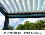 Small photo of Trendy outdoor patio pergola. sky and clouds pass through the metallic structure. green trees in the background
