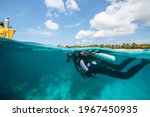 Small photo of A scuba diver swimming back to the boat on a tropical island of Utila, Bay Islands, Honduras, Central America, over-under photo, split shot, splits, Carribean sea diver, PADI, SSI certified diver