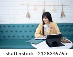 Asian Woman with black hair working comfortably with a tablet  drinking hot coffee.A young Asian girl sits at work relaxing with her favorite cup of coffee.Business woman enjoying to drink beverage.