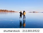 A young couple is skating on the frozen Lake Baikal. Transparent ice. Travel in winter, active recreation, sports. 