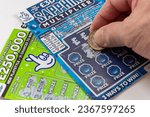 Small photo of London. UK- 09.27.2023. Two National Lottery scratch cards isolated in white with a player scratching a card with a coin.