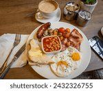A plate of full English breakfast served on a table with a cup of coffee.