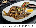 Small photo of fried flounder on a plate with sauce on dark stone table