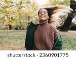 Charming joyful woman running in motion in public park. Attractive smiling woman swinging her hair outdoors during the sunny fall day.