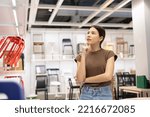 Small photo of Young beautiful woman choosing the right chair furniture for her house at showroom. Female looking and thinking near lot of armchair at furniture store hall. Buying various item for new house