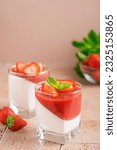 Small photo of Panna cotta homemade Italian dessert of sweetened cream thickened with gelatin with layer or fresh strawberry sauce decorated with juicy berries and mint leaf served in glass on table with ingredients