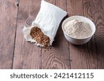 Small photo of Buckwheat in a canvas bag and buckwheat flour in a bowl on a wooden table. Gluten free buckwheat flour.