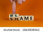 Small photo of Blame or shame. Male hand flips wooden cubes and changes the word 'shame' to 'blame' or vice versa. Beautiful orange background, copy space. Blame or shame concept.