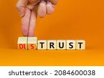 Small photo of Distrust or trust symbol. Businessman turns wooden cubes, changes words 'distrust' to 'trust'. Beautiful orange table, orange background. Business and distrust or trust concept, copy space.