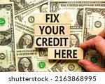 Small photo of Fix your credit here symbol. Concept words Fix your credit here on wooden blocks on a beautiful background from dollar bills. Businessman hand. Business, finacial and fix your credit here concept.