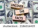 Small photo of Uncover the facts symbol. Concept words Uncover the facts on wooden blocks on a beautiful background from dollar bills. Business and uncover the facts concept. Copy space.
