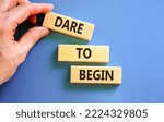 Small photo of Dare to begin symbol. Wooden blocks with words 'Dare to begin'. Beautiful blue background, businessman hand. Business, dare to begin concept, copy space.