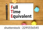 Small photo of FTE Full time equivalent symbol. Concept words FTE Full time equivalent on white note. Beautiful wooden table wooden background. Business and FTE Full time equivalent concept. Copy space.